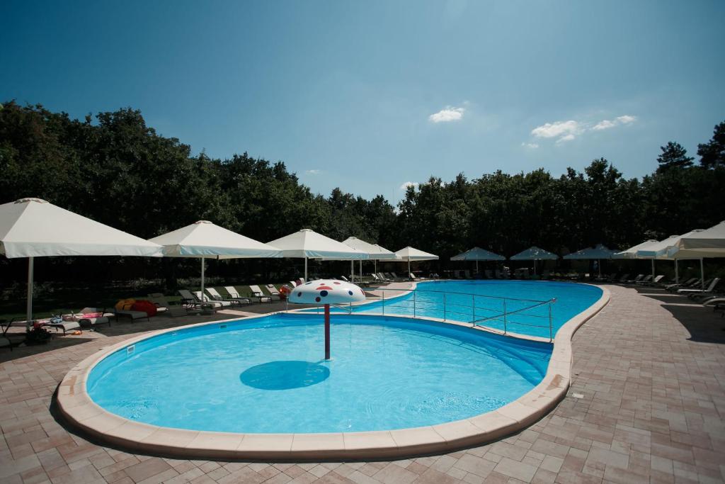une grande piscine avec des parasols blancs et des chaises dans l'établissement Forrest Park&Resort, à Orlovshchina