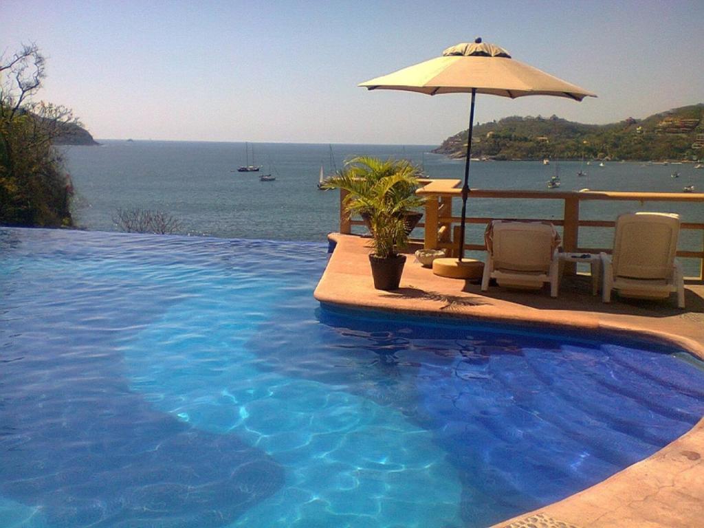 a swimming pool with an umbrella and a view of the ocean at Hotel Irma in Zihuatanejo