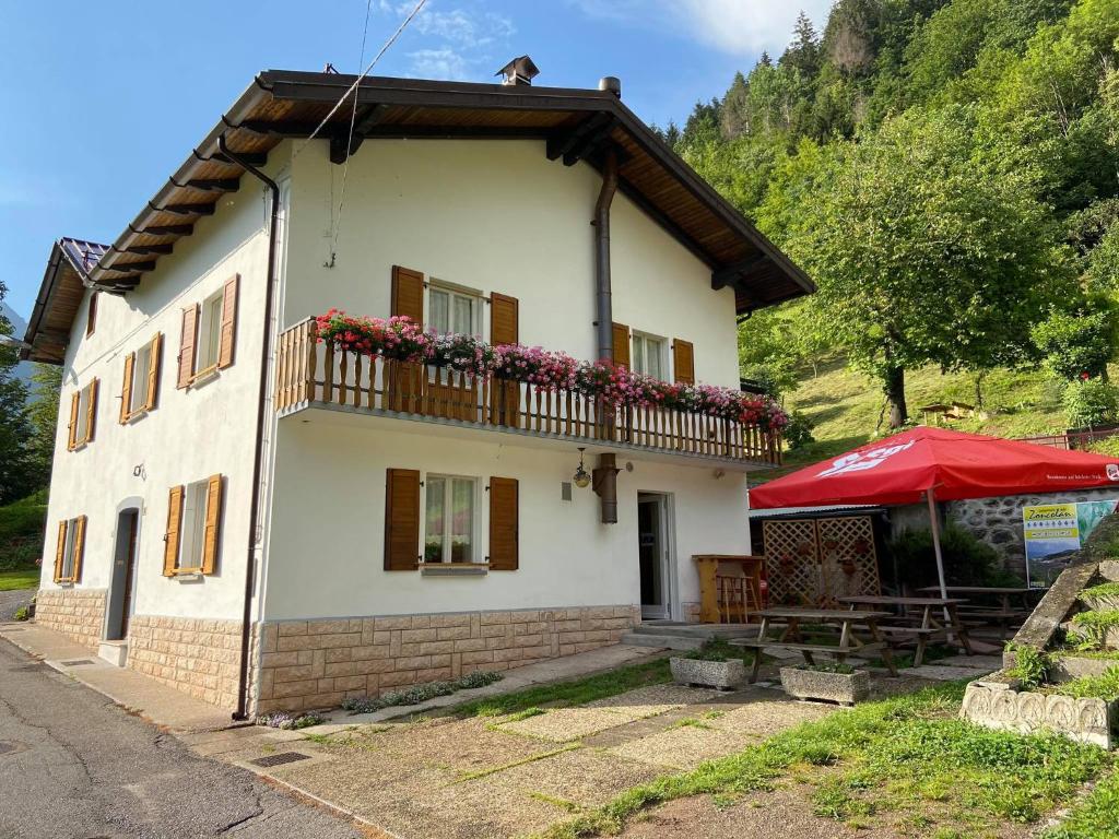 a white house with a balcony and a red umbrella at Casa Ortis in Paluzza