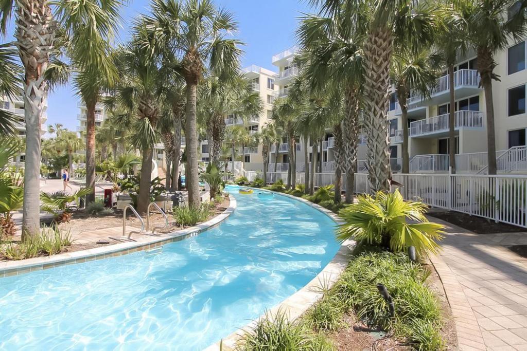 a swimming pool with palm trees in front of a building at Destin West Resort in Fort Walton Beach