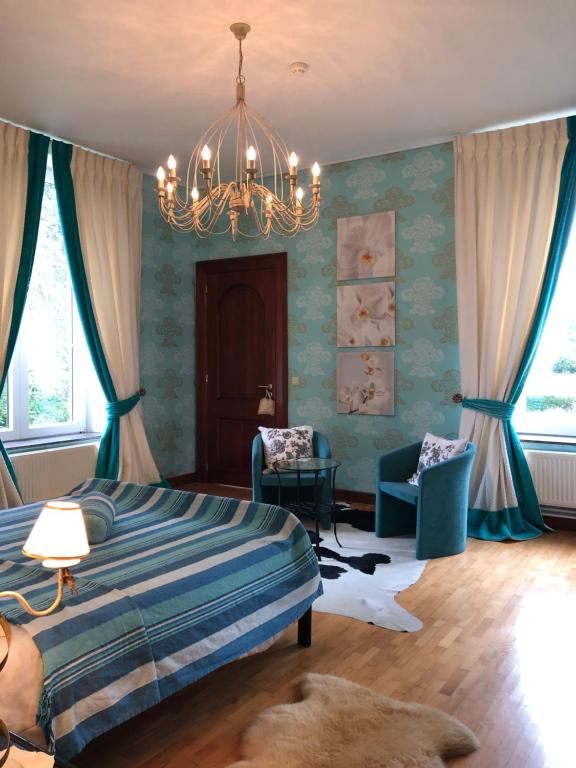 a bedroom with a bed and two chairs and a chandelier at Château Les Tourelles in Bertrix