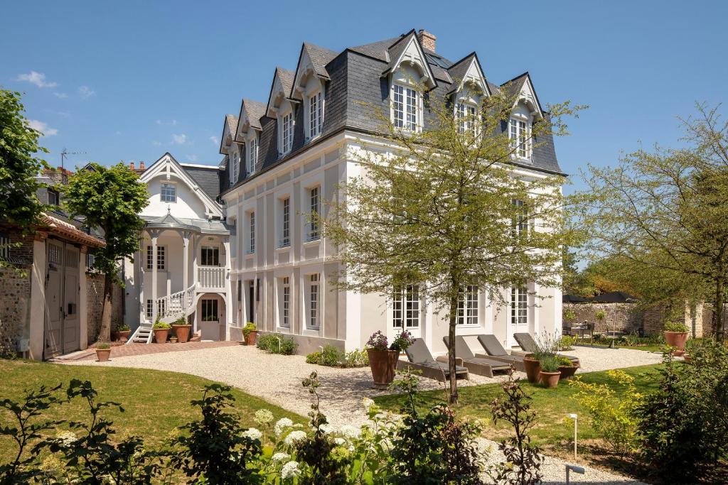 Cette grande maison blanche dispose d'une cour avec des chaises. dans l'établissement Hôtel Saint-Delis - La Maison du Peintre - Relais & Châteaux, à Honfleur