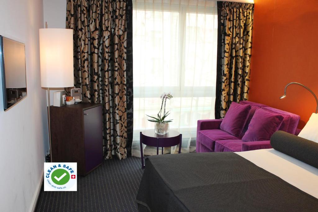 une chambre d'hôtel avec un lit et un canapé violet dans l'établissement The New Midi, à Genève
