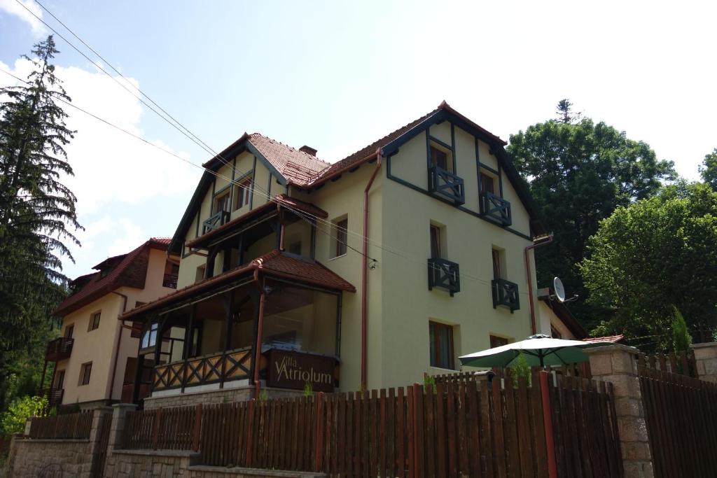 una casa amarilla con una valla y una sombrilla en Villa Atriolum, en Băile Tuşnad