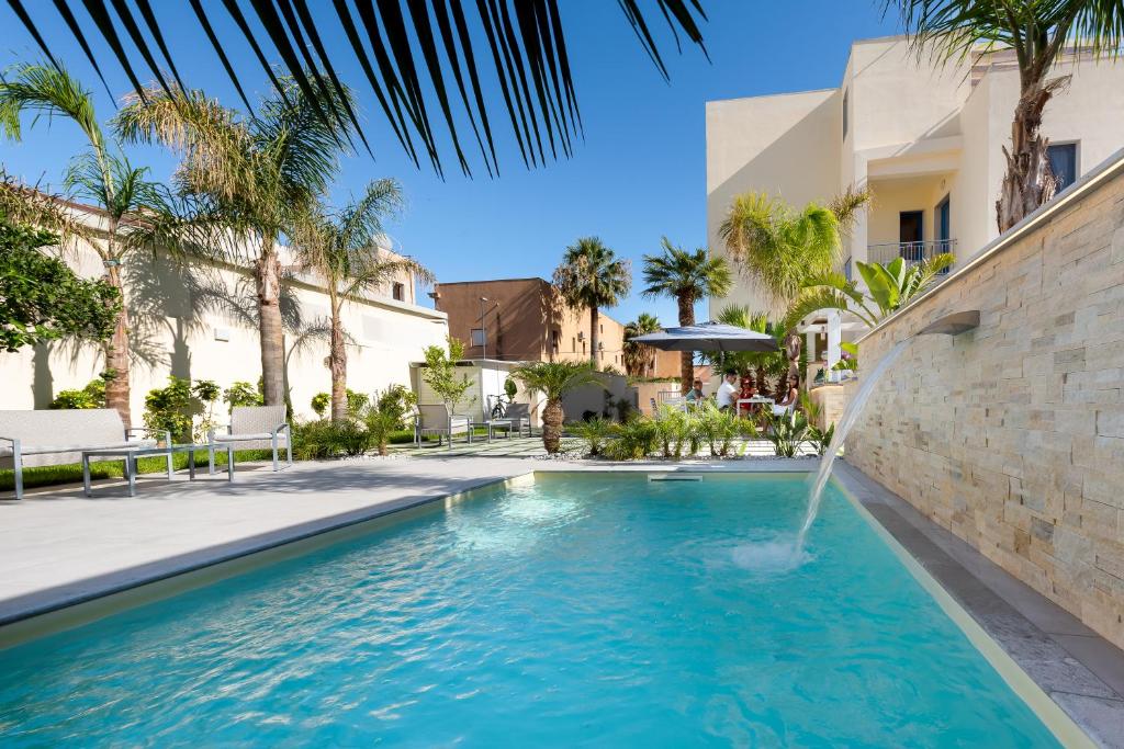 a swimming pool with a fountain in a courtyard with palm trees at Fior di Lino Rooms in San Vito lo Capo