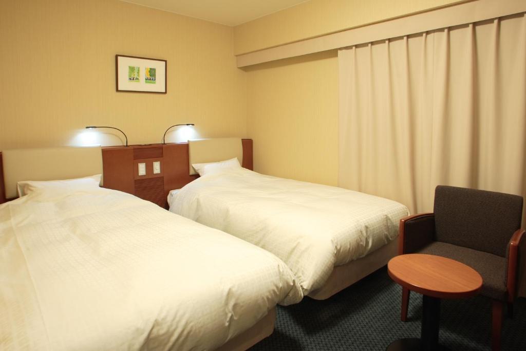 a hotel room with two beds and a chair at Smile Hotel Sendai-Kokubuncho in Sendai