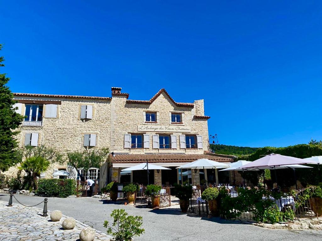 un grand bâtiment avec des tables et des parasols devant lui dans l'établissement Auberge du Vieux Château, à Cabris