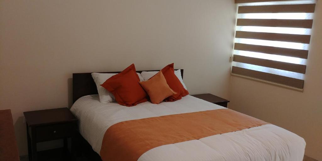 a bedroom with a bed with orange pillows and a window at Hotel Lorimar in La Paz