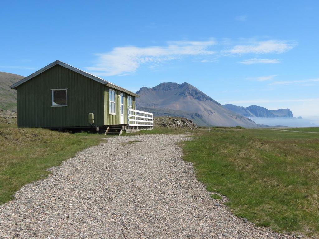 een groen huis op een grindweg met bergen op de achtergrond bij Stafafell Cottages in Stafafell