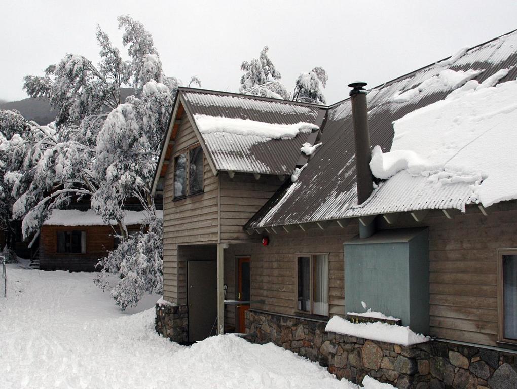 a house covered in snow with trees in the background at Bollygums in Thredbo