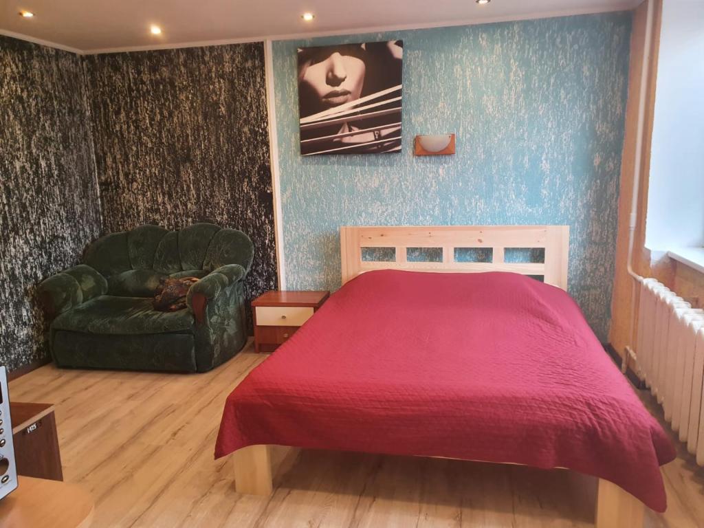 a bedroom with a red bed and a green chair at Apartament Erfolg 3 in Daugavpils