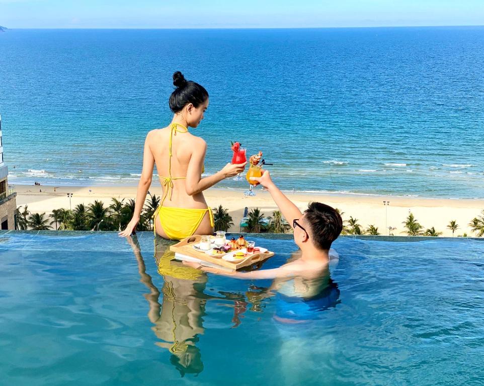 a woman giving a man a drink in a swimming pool at Santa Luxury Hotel in Da Nang