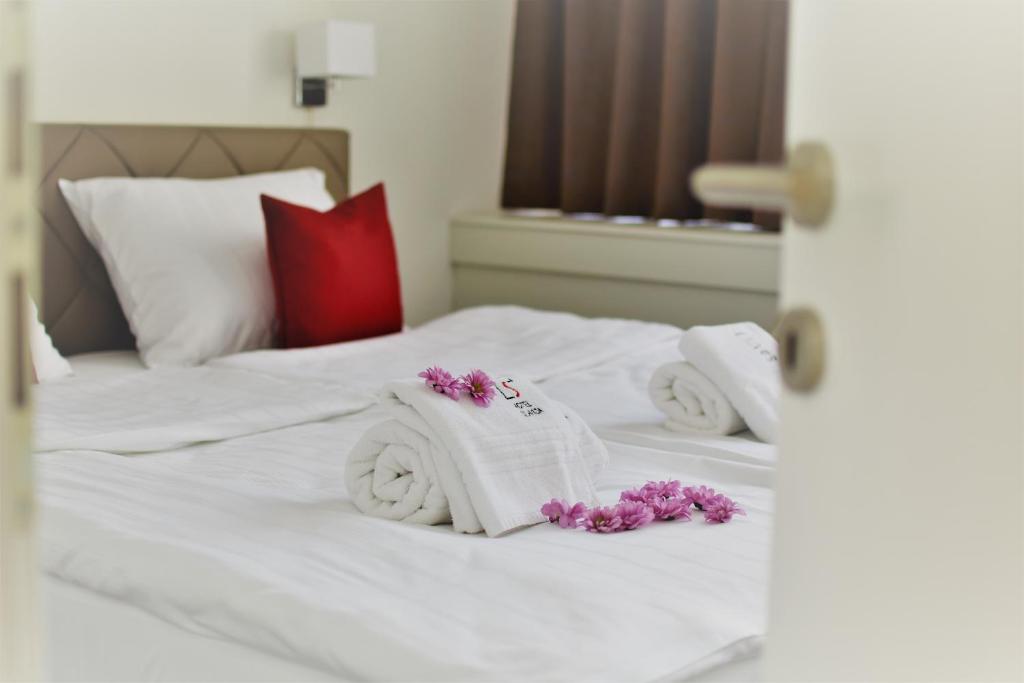 a white bed with towels and purple flowers on it at Hotel Slavija Banja Luka in Banja Luka