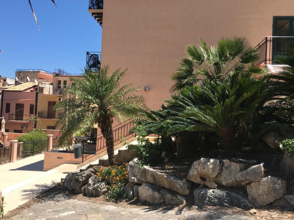 a garden with palm trees and rocks in front of a building at Castellammare Smart Rooms in Castellammare del Golfo