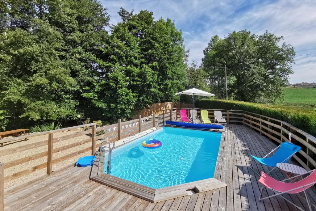 - une piscine avec des chaises et un parasol sur une terrasse en bois dans l'établissement Gite du Moulin Toucan, à Berneuil