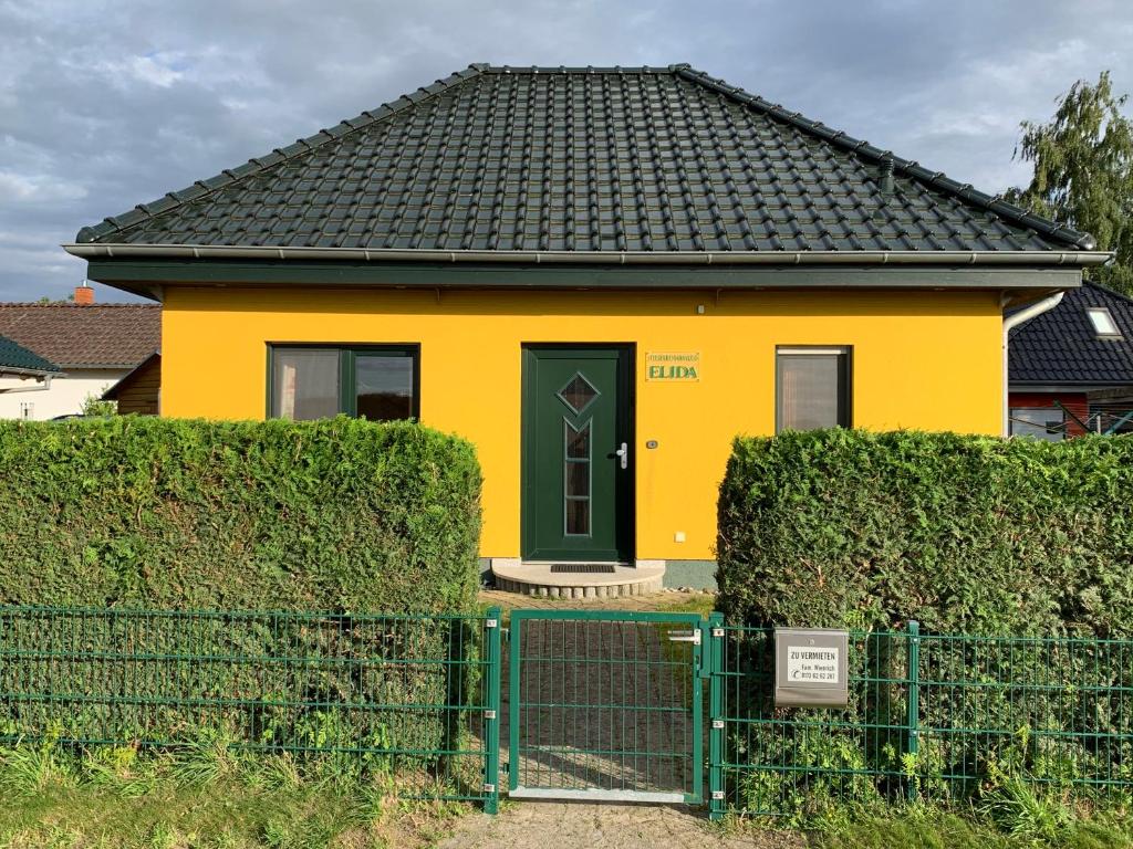 żółty dom z czarnymi drzwiami i płotem w obiekcie Ferienhaus Elida w mieście Krummin