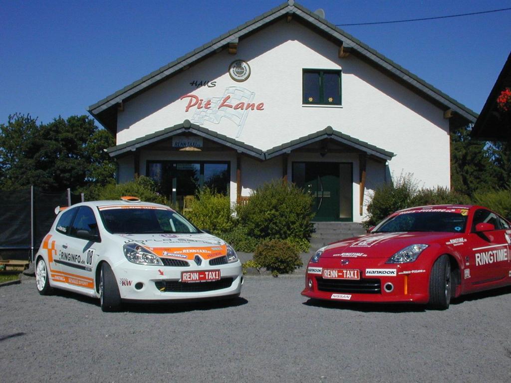 zwei Autos auf einem Parkplatz vor einem Gebäude geparkt in der Unterkunft Hotel Pit Lane "Home of Motorsport" in Nürburg
