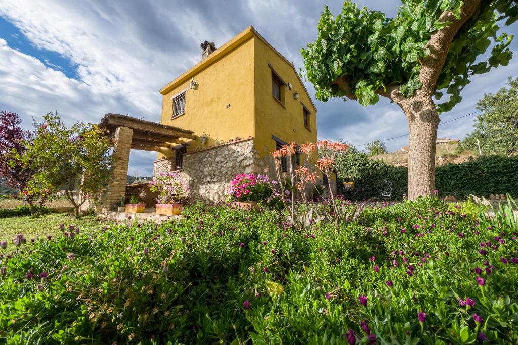 a yellow house with a tree and flowers at Casa rural lo Maset de Carmeta in Tivenys