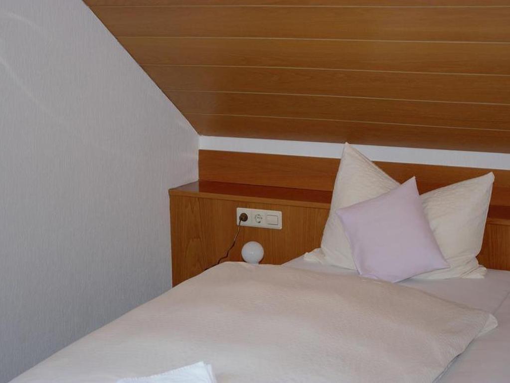 um quarto com uma cama com lençóis brancos e almofadas em Hotel Garni Silberdistel em Nenningen