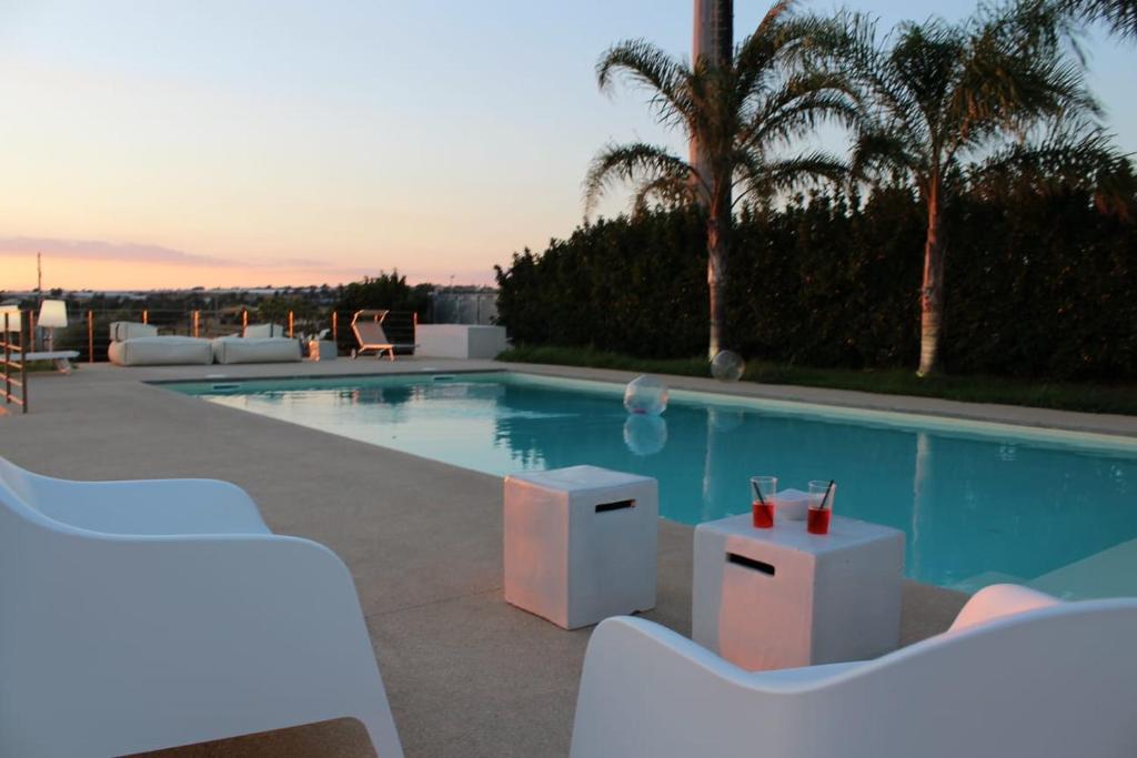 einen Pool mit weißen Stühlen neben einem Pool in der Unterkunft Casa Antea in Marina di Ragusa