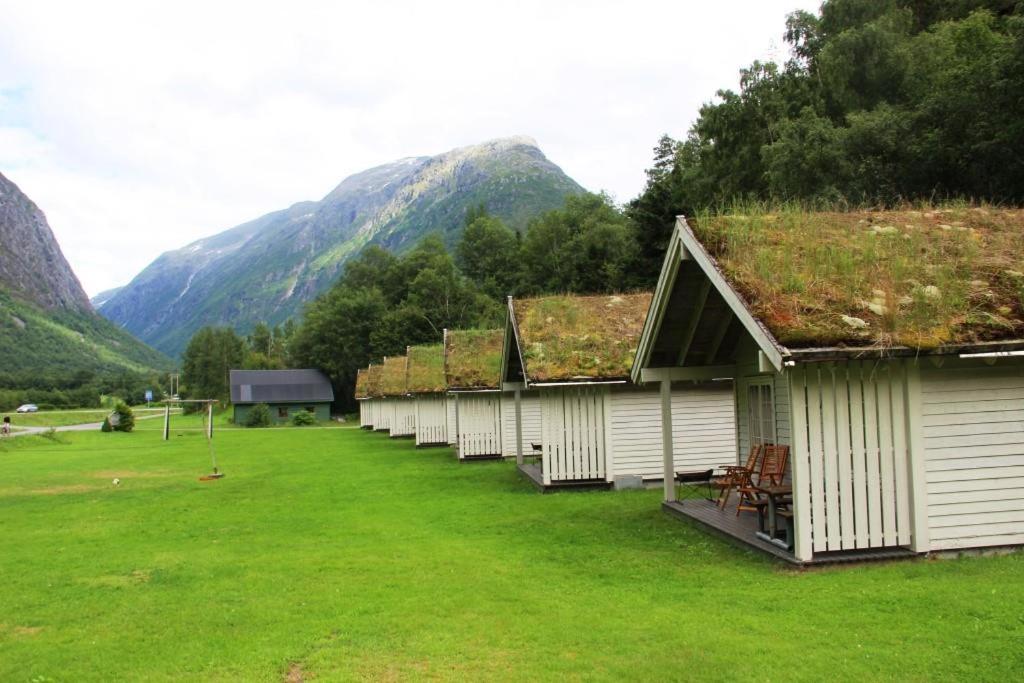 una fila di case con tetti d'erba con montagne sullo sfondo di Hjelledalen Hyttesenter a Hjelle