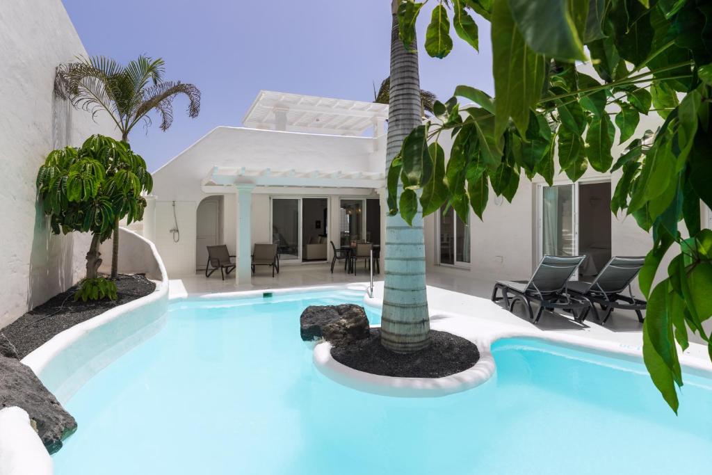 een zwembad met een palmboom voor een huis bij Bahiazul Villas Corralejo by Vreagestion in Corralejo