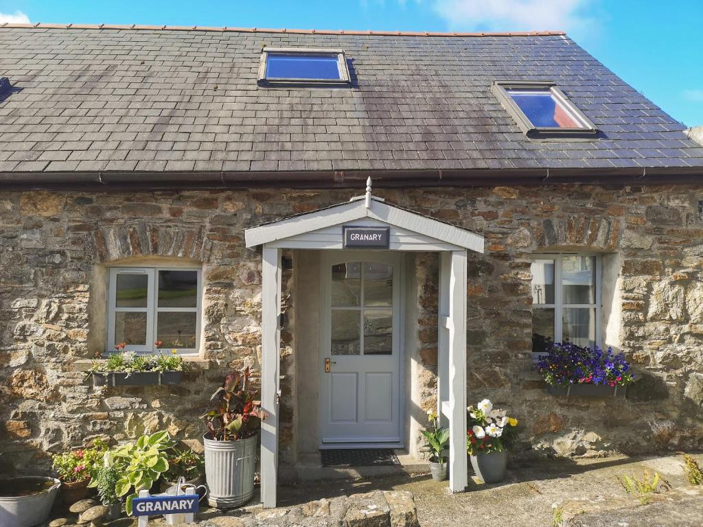 a stone cottage with a white door and windows at The Granary in Llandyfrydog