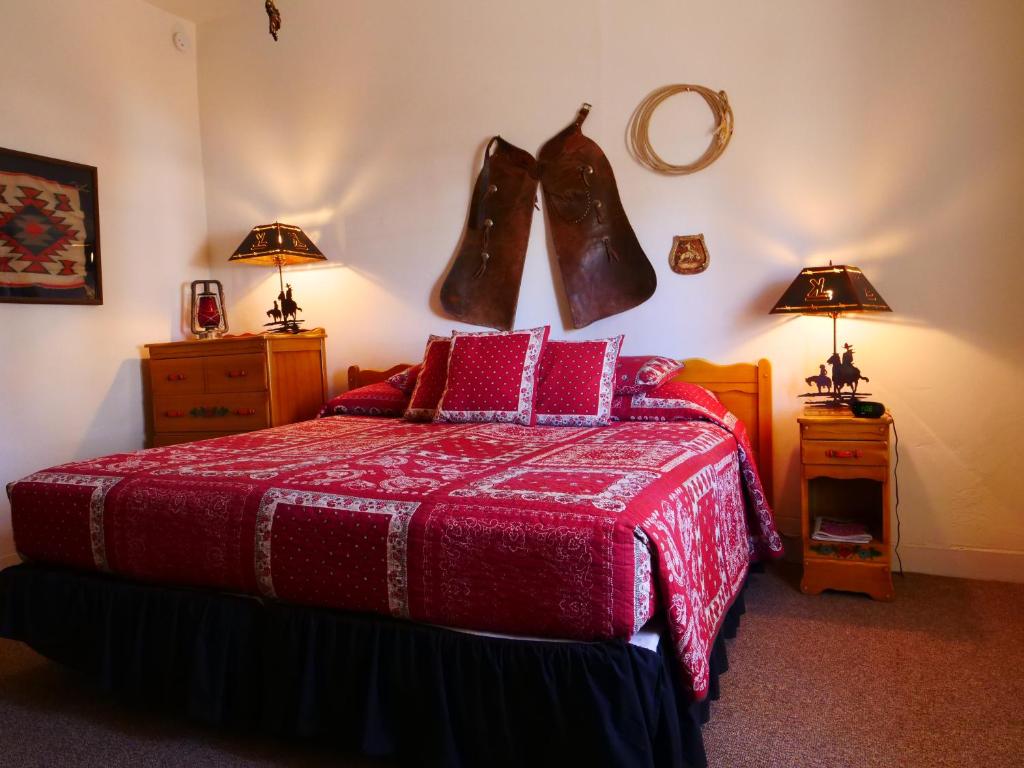 a bedroom with a bed with a red blanket and boots on the wall at Kay El Bar Guest Ranch in Wickenburg