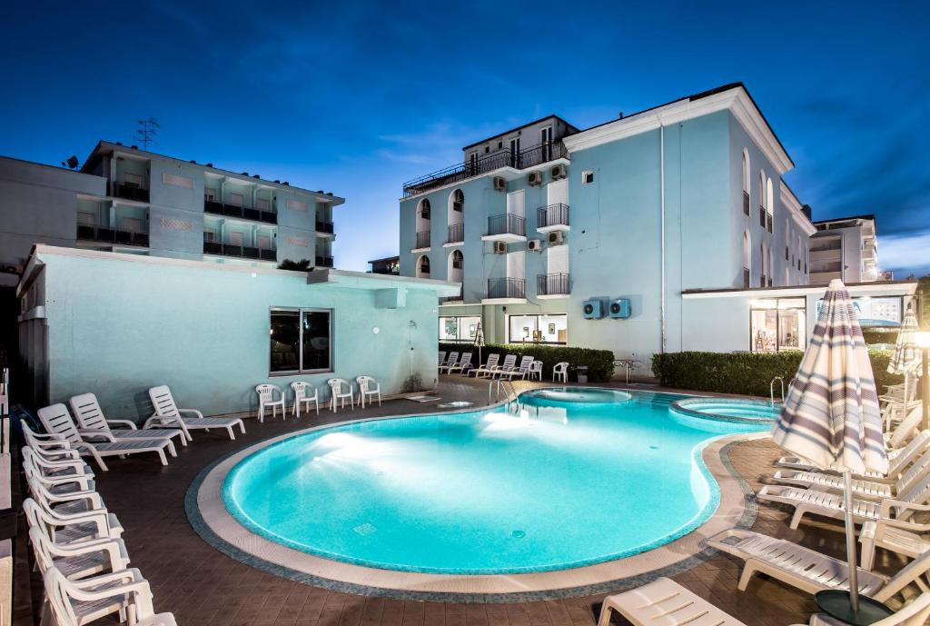une piscine avec des chaises longues et un hôtel dans l'établissement Adriatico Family Village, à Gatteo a Mare