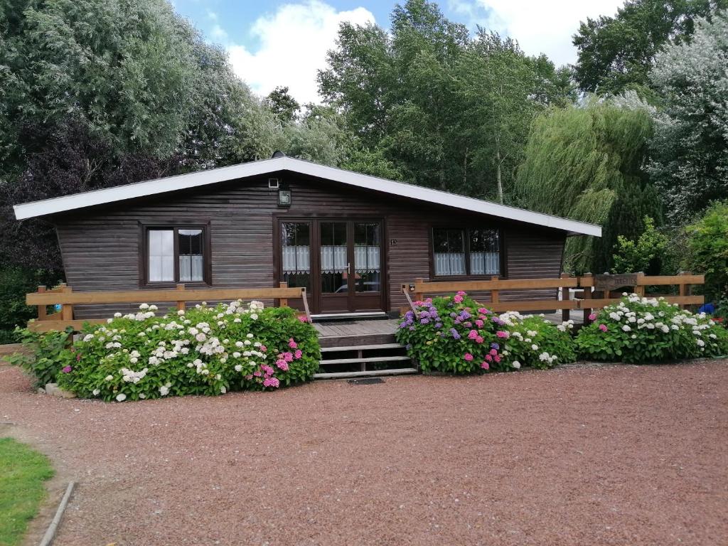 Cabaña de madera pequeña con banco y flores en Chalet de vacances, en Guisy