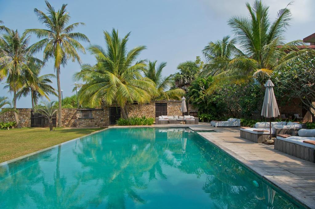 a swimming pool in front of a house with palm trees at Knai Bang Chatt Resort in Kep