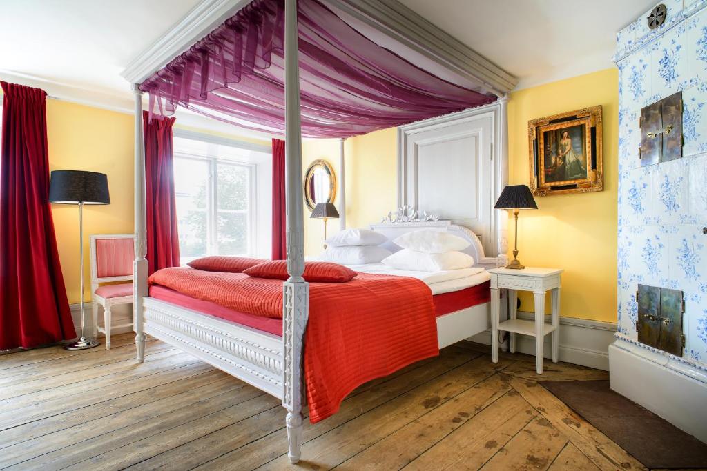 a bedroom with a canopy bed with a red blanket at Hotel Hellstens Malmgård in Stockholm