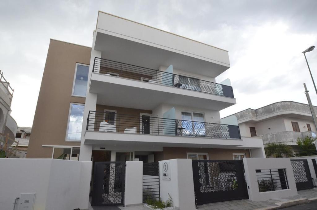 wysoki biały budynek z płotem przed nim w obiekcie Riva 33 Apartments w mieście Porto Cesareo