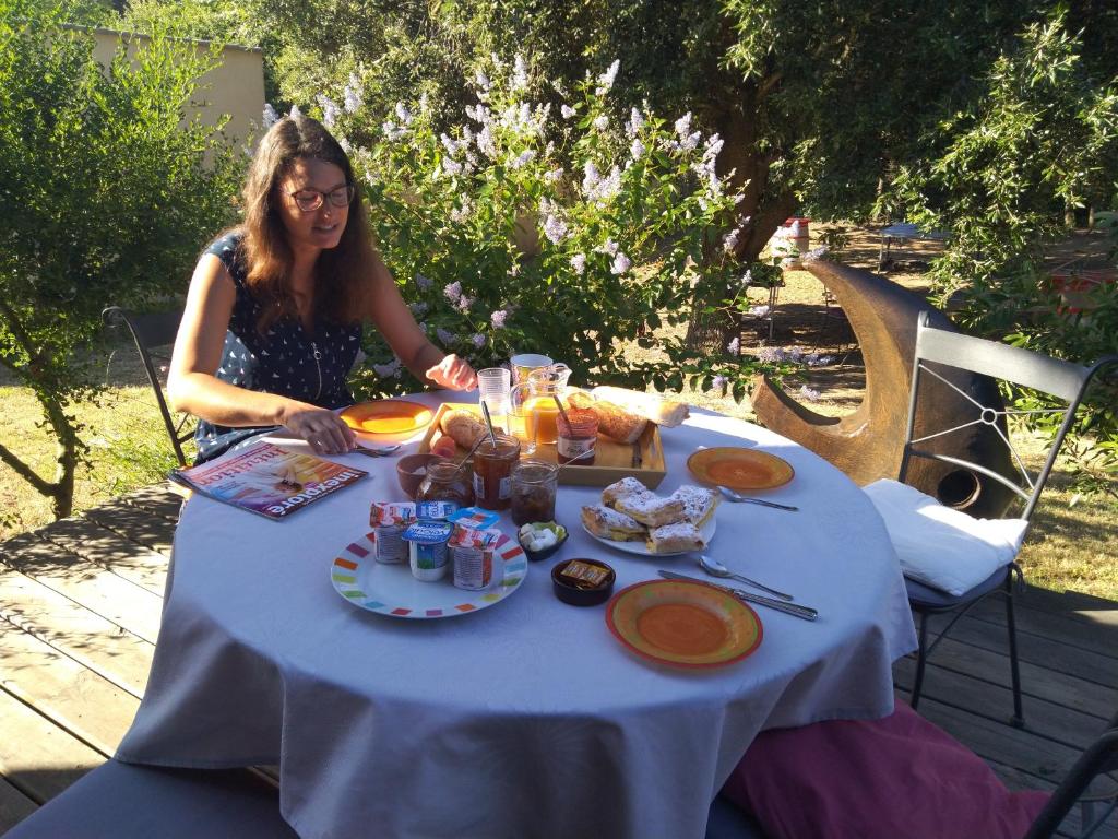 a woman sitting at a table with food on it at Chambre d’Hôtes Neptune Wood in Arzens