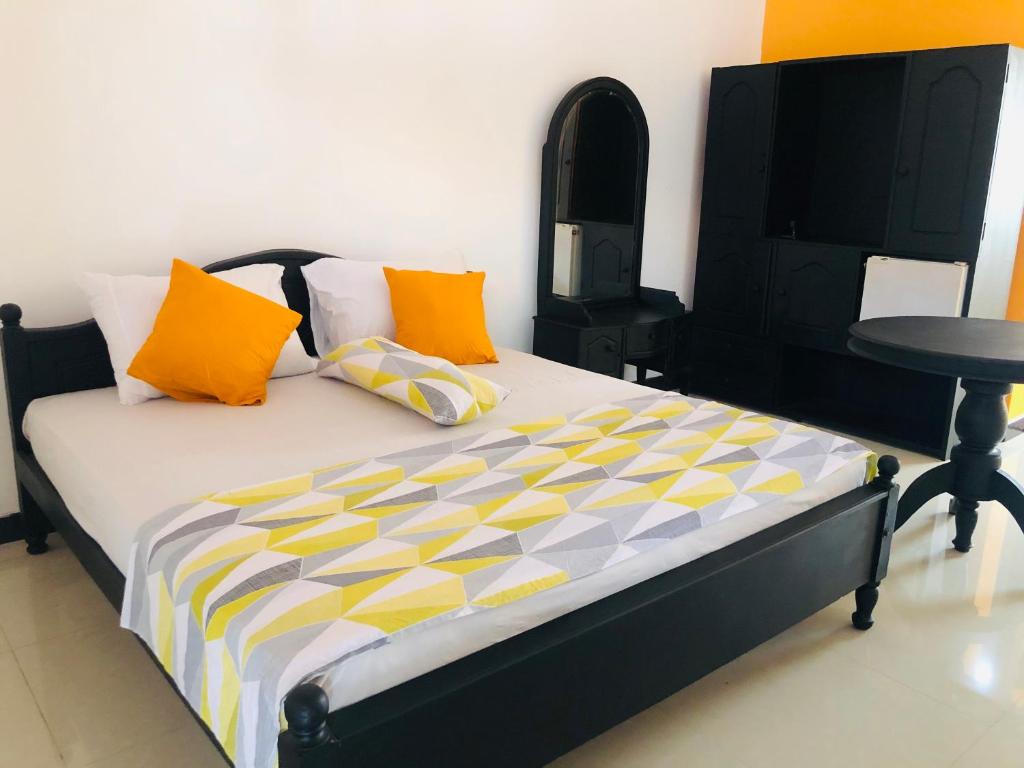 a bed with orange and yellow pillows and a table at Grand Camellia Hotel in Ambalantota