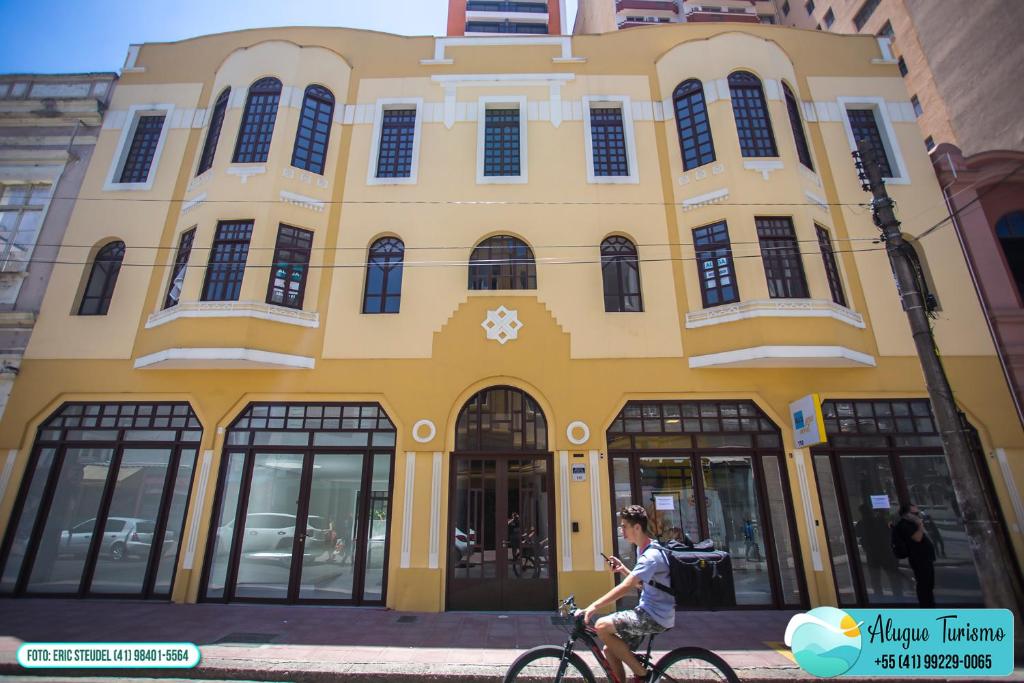 une femme à vélo devant un bâtiment jaune dans l'établissement Apartamento 615 - All You Need, à Curitiba