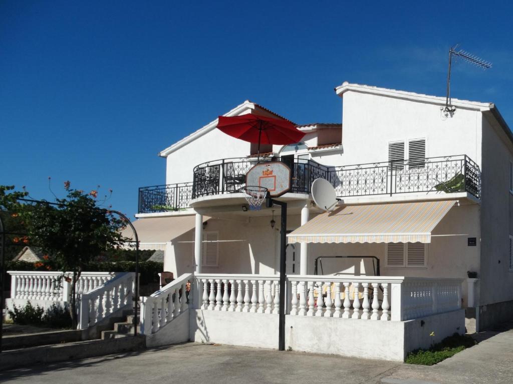 un edificio blanco con un aro de baloncesto y una sombrilla en Primošten Apartman Dino en Primošten