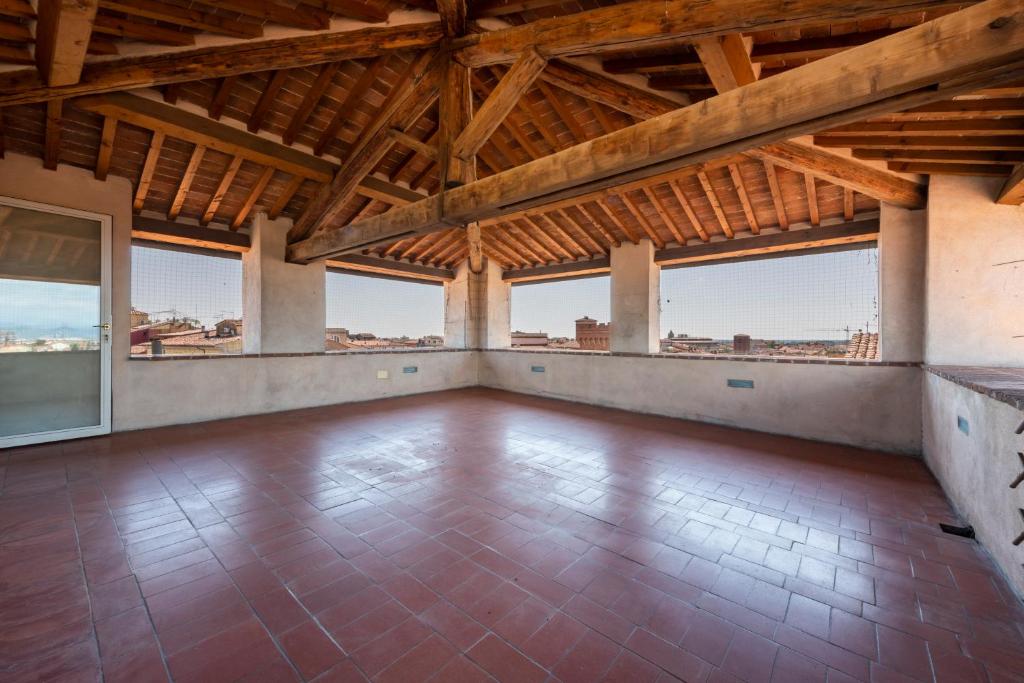 an empty room with wooden ceilings and large windows at Nella Torre del Poschi Penthouse with Roof Terrace in Pisa
