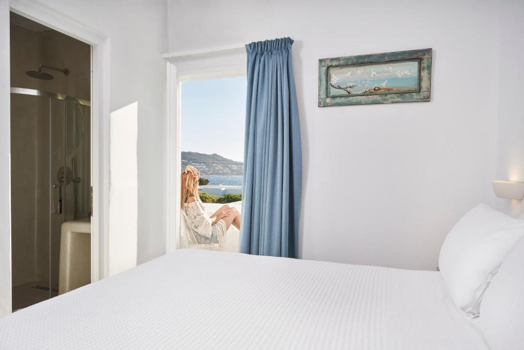 a woman looking out the window of a bedroom at Galation in Mýkonos City