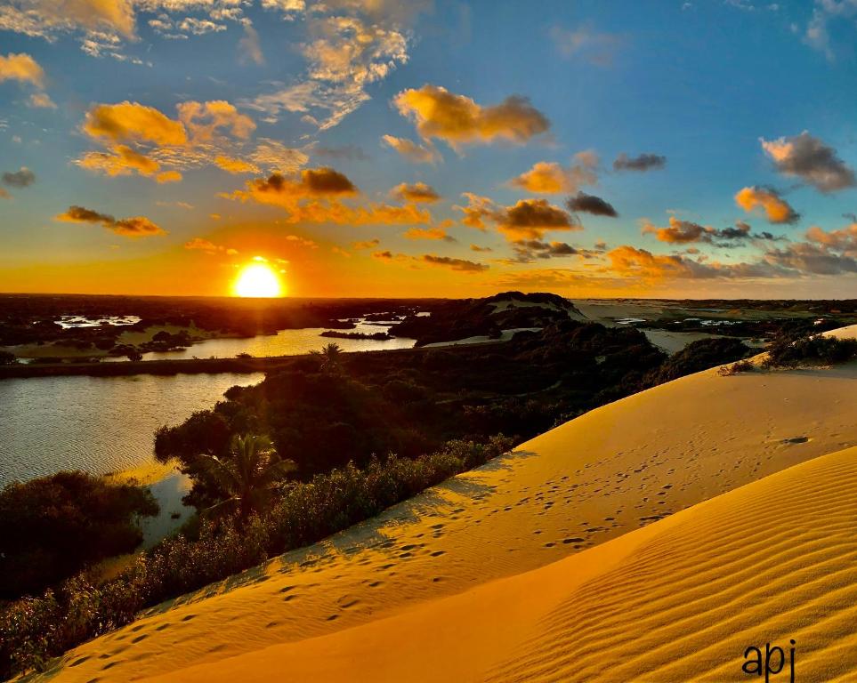 Pousada Ponta dos Anéis في مراكاجو: غروب الشمس في الصحراء مع نهر وكثبان رملي