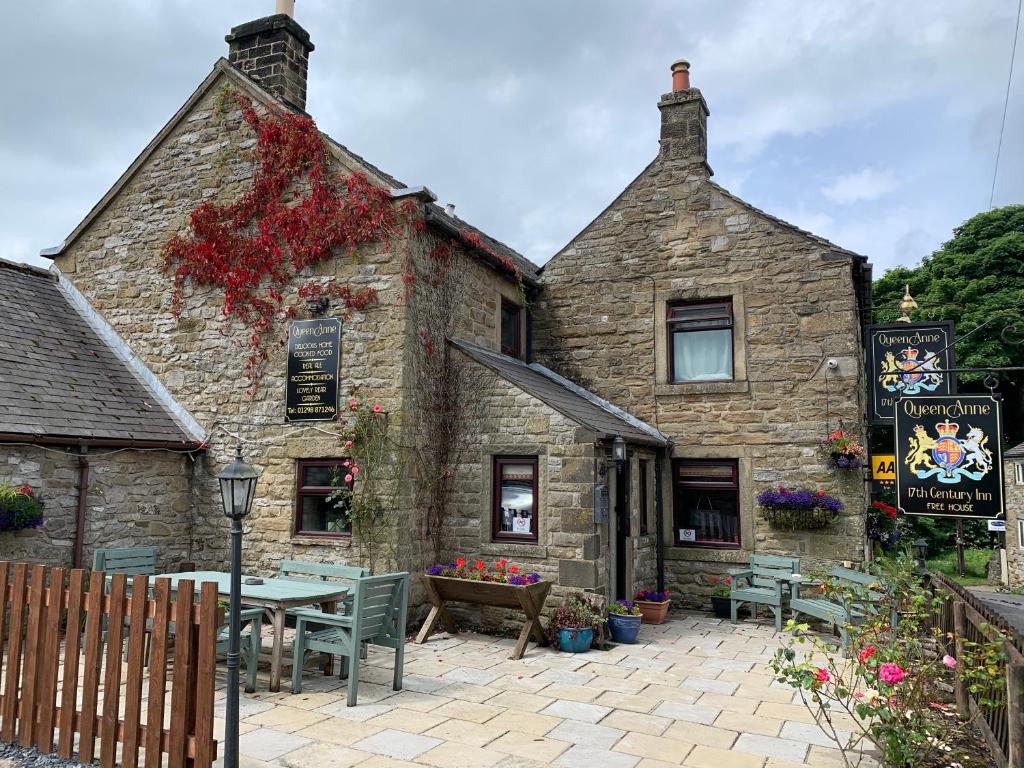 un edificio de piedra con una mesa y sillas delante de él en The Queen Anne, en Hucklow