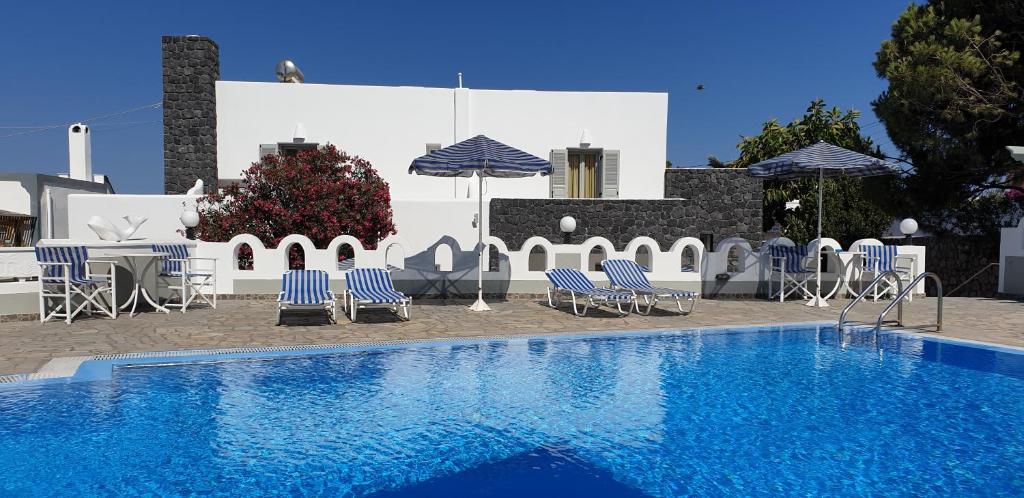 a swimming pool with chairs and umbrellas next to a building at Atlas Pension in Karterados