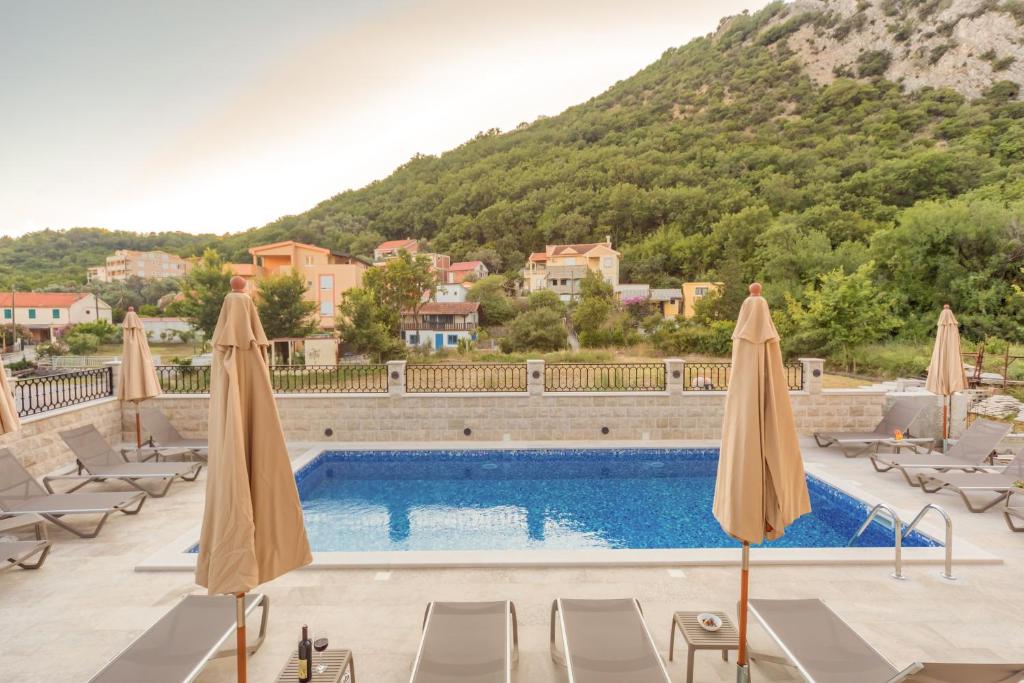 a pool with chairs and umbrellas in front of a mountain at Luxury Apartments Queen in Petrovac na Moru
