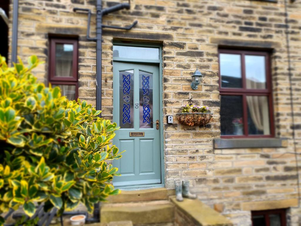 een bakstenen huis met een blauwe deur en twee ramen bij Bronte Railway Cottage at Haworth in Haworth