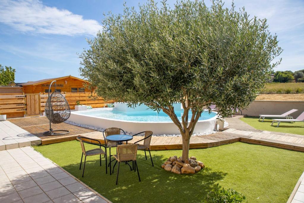 une table et des chaises sous un arbre à côté d'une piscine dans l'établissement Le chalet aux Etoiles Spa & Sauna, à Pézenas