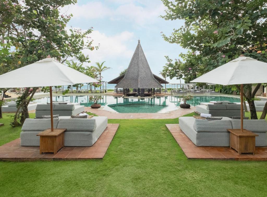 a lawn with couches and umbrellas next to a pool at Sadara Resort in Nusa Dua