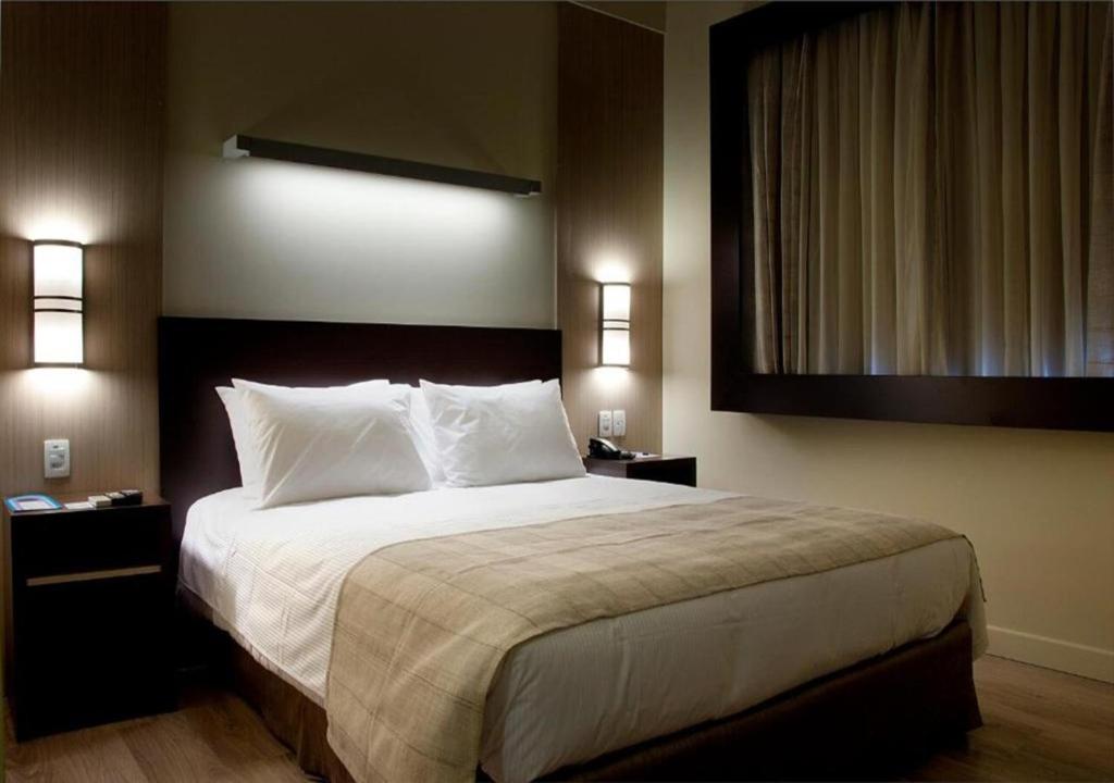 a hotel room with a bed and a lamp at Master Cosmopolitan Moinhos de Vento in Porto Alegre