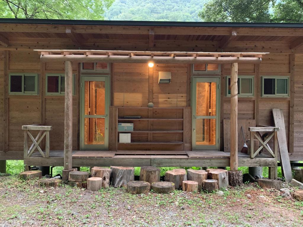 Cabaña de madera con porche y algunos troncos en YAMAYA BASE 1, en Ōkawamochi