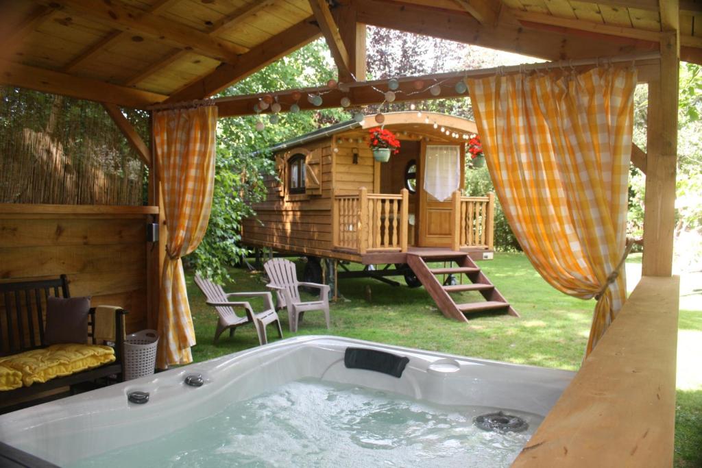 uma banheira de hidromassagem num quintal com uma casa na árvore em La Roulotte d'Emilie et son jacuzzi privé em Beurlay