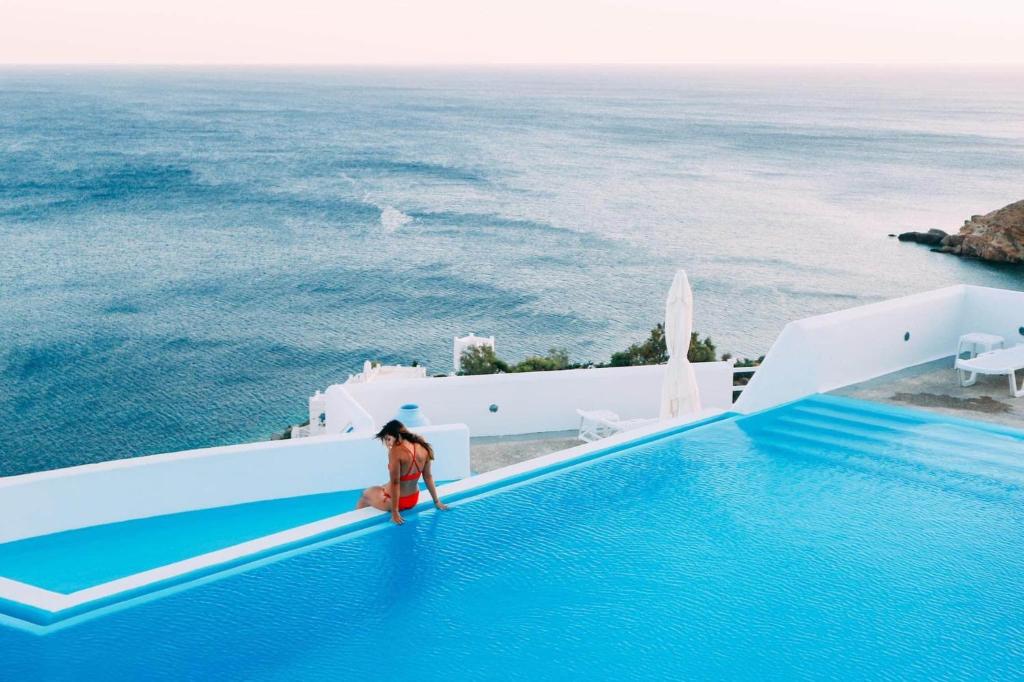 a woman standing on the edge of a swimming pool overlooking the ocean at Hotel Petradi in Ios Chora